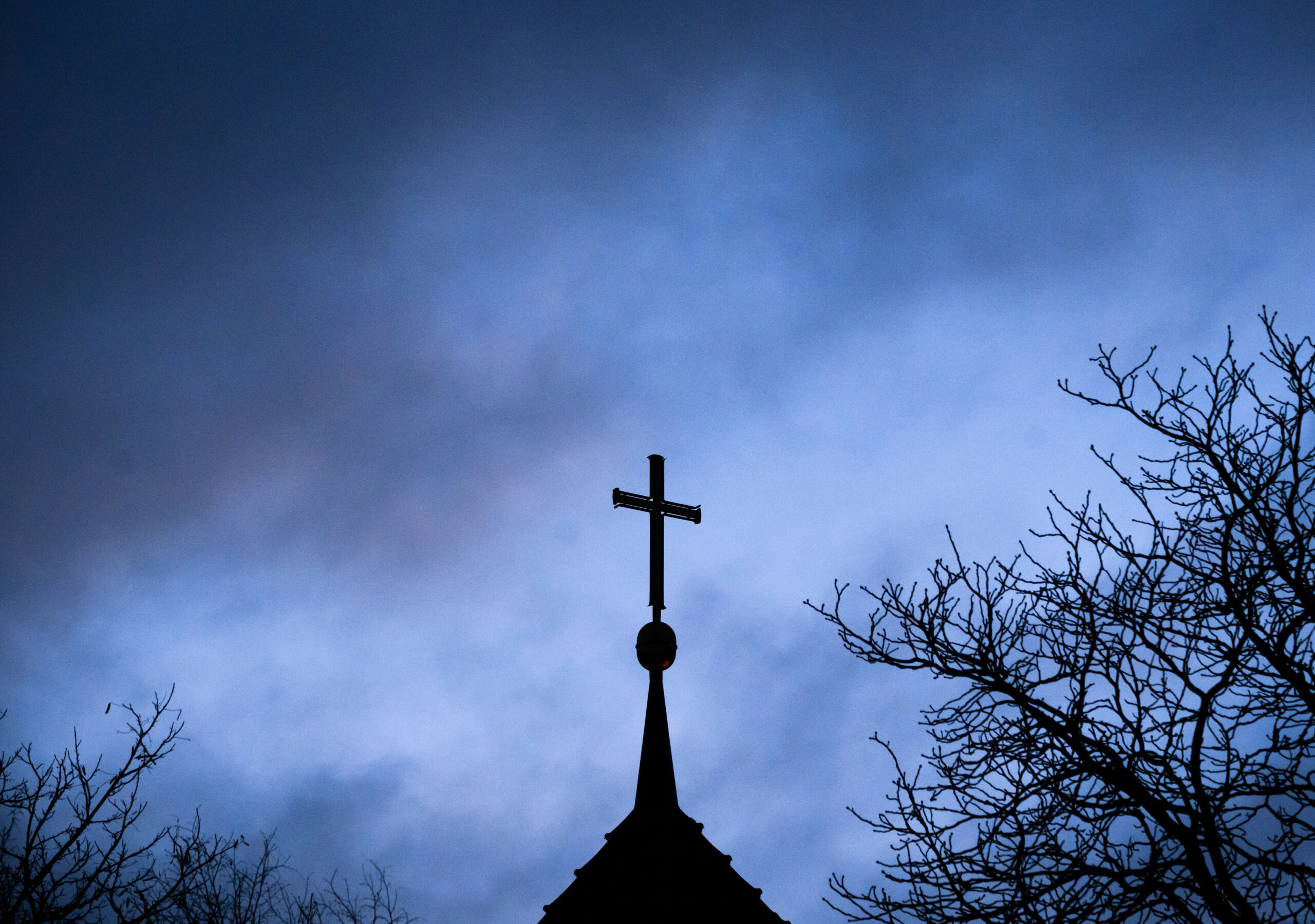 Dunkle Wolken ziehen über das Kreuz auf einer evangelischen Kirche hinweg