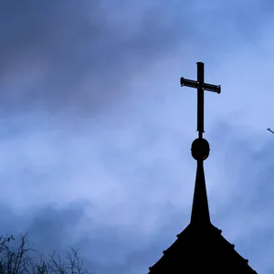 Dunkle Wolken ziehen über das Kreuz auf einer evangelischen Kirche hinweg