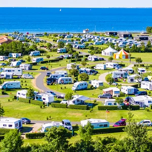 Das „Insel-Camp“ auf Fehmarn. Im Hintergrund ist blauer Himmel und blaues Meer. Man sieht viele weiße Wohnwagen/ Wohnmobile.