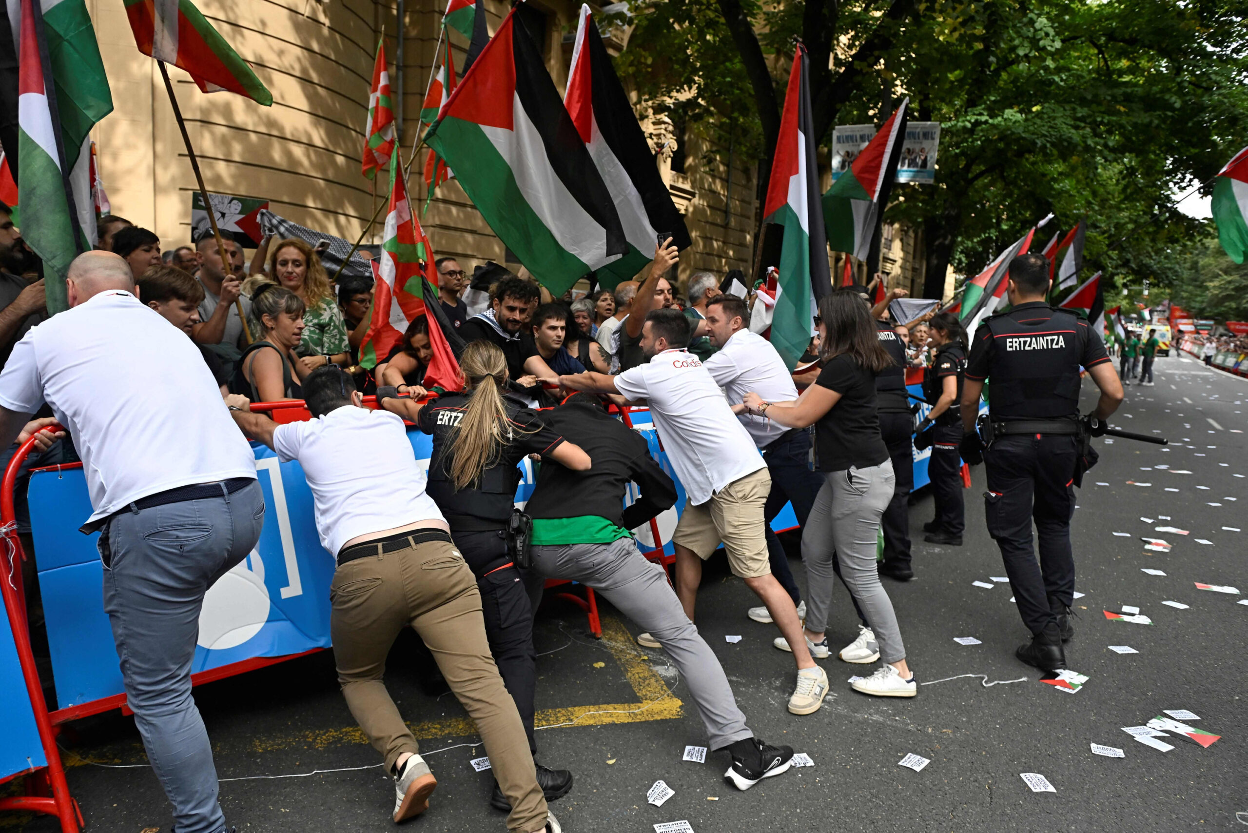 Pro-Palästina-Demonstranten versuchen eine Absperrung zu durchbrechen. Die baskische Polizei und Mitarbeiter der Radsport-Teams versuchen, dies zu verhindern.