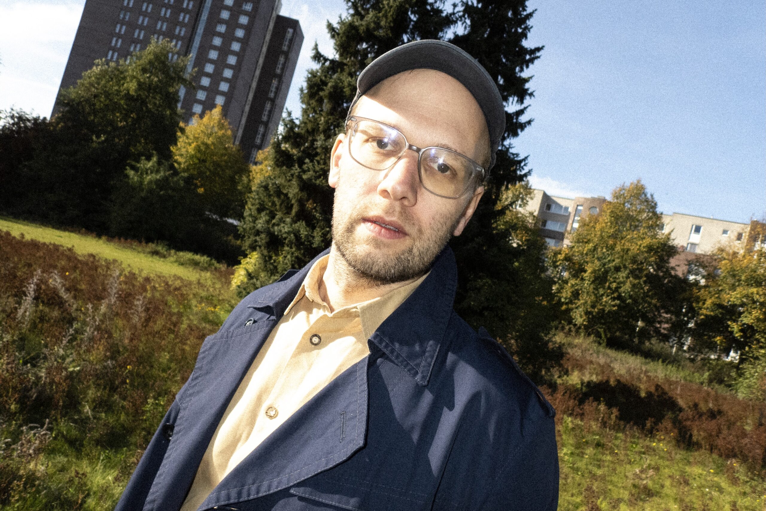 Er steht draußen, im Hintergrund Grün und Häuser