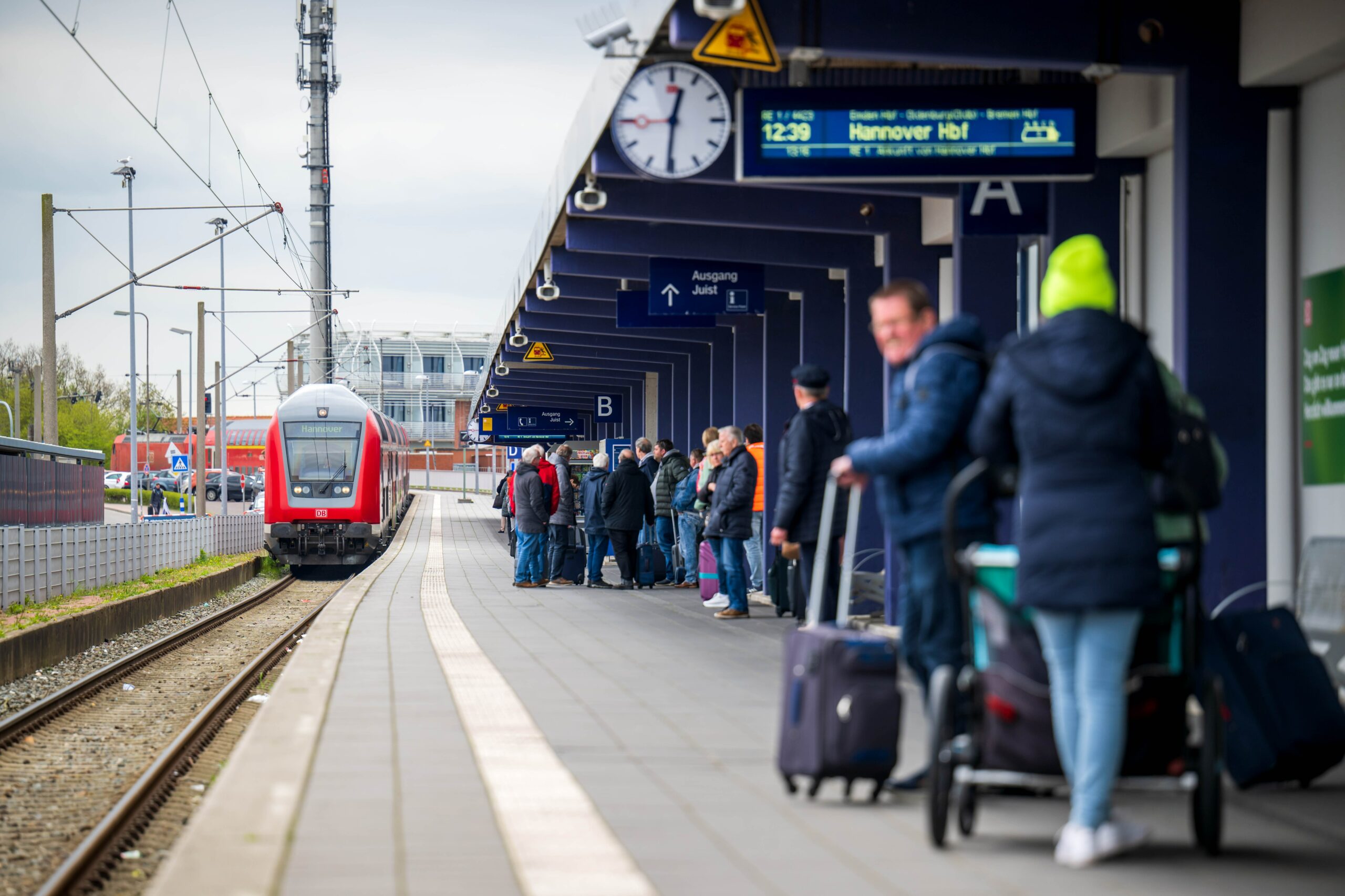 Touristen laufen mit Rollkoffern am Bahnhof Norddeich-Mole entlang.