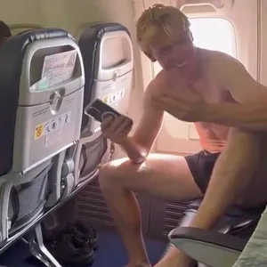 Ein junger Mann sitzt in Unterwäsche im Flugzeug und lacht