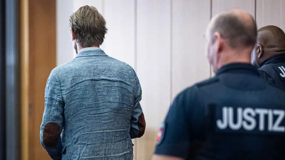 Christian B. steht mit dem Rücken zur Kamera, links sind zwei Justizbeamte