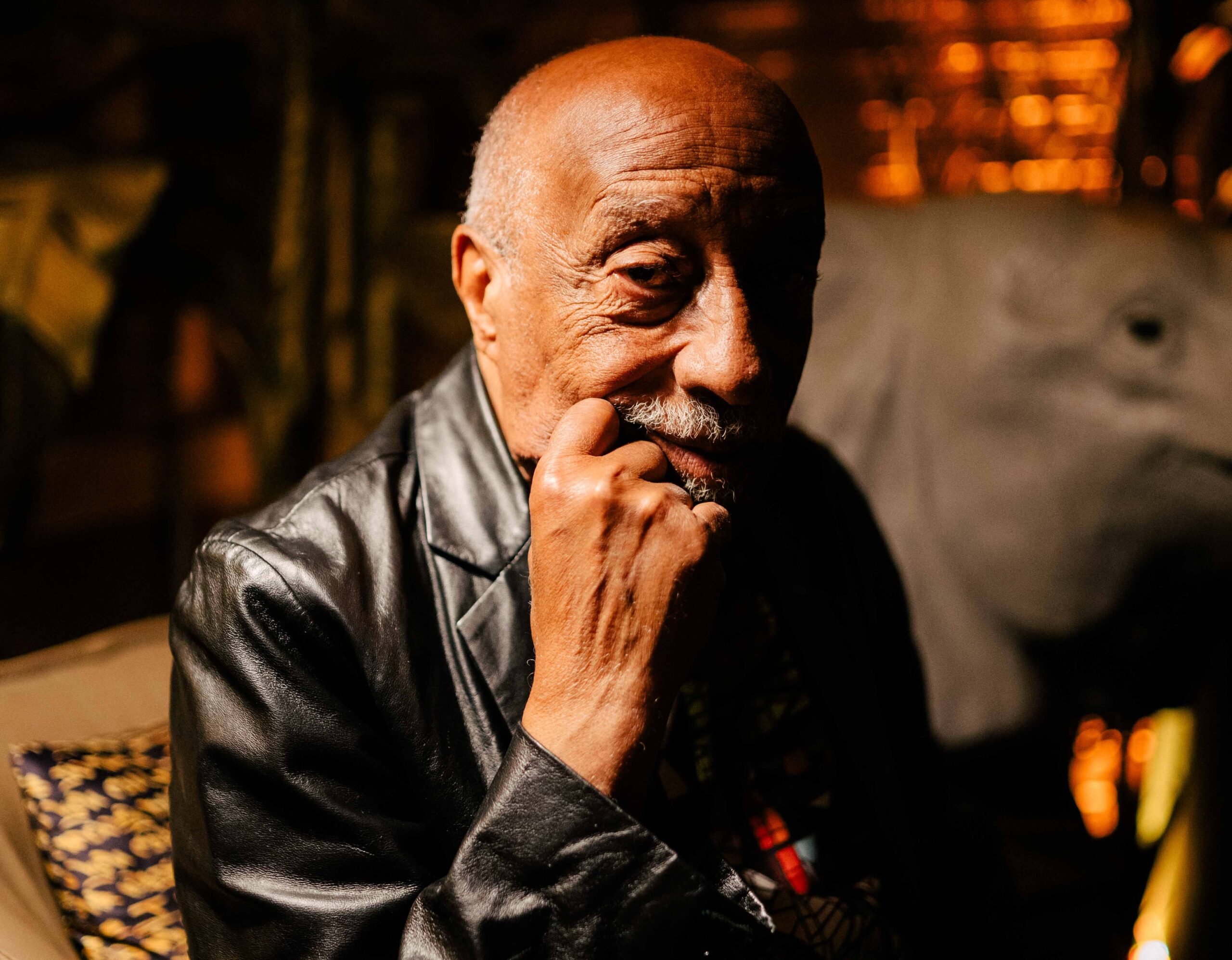 Er schaut in die Kamera, den Kopf auf eine Hand gestützt