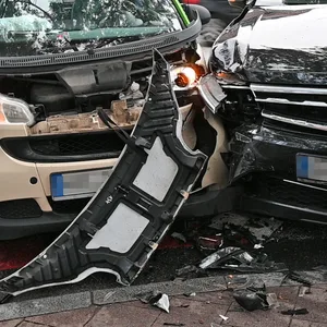 Zwei Autos stehen am Straßenrand. Die Fahrzeugfronten sind an der einen Seite aneinander gedrüclkt. Beide Fahrzeuge sind stark beschädigt.