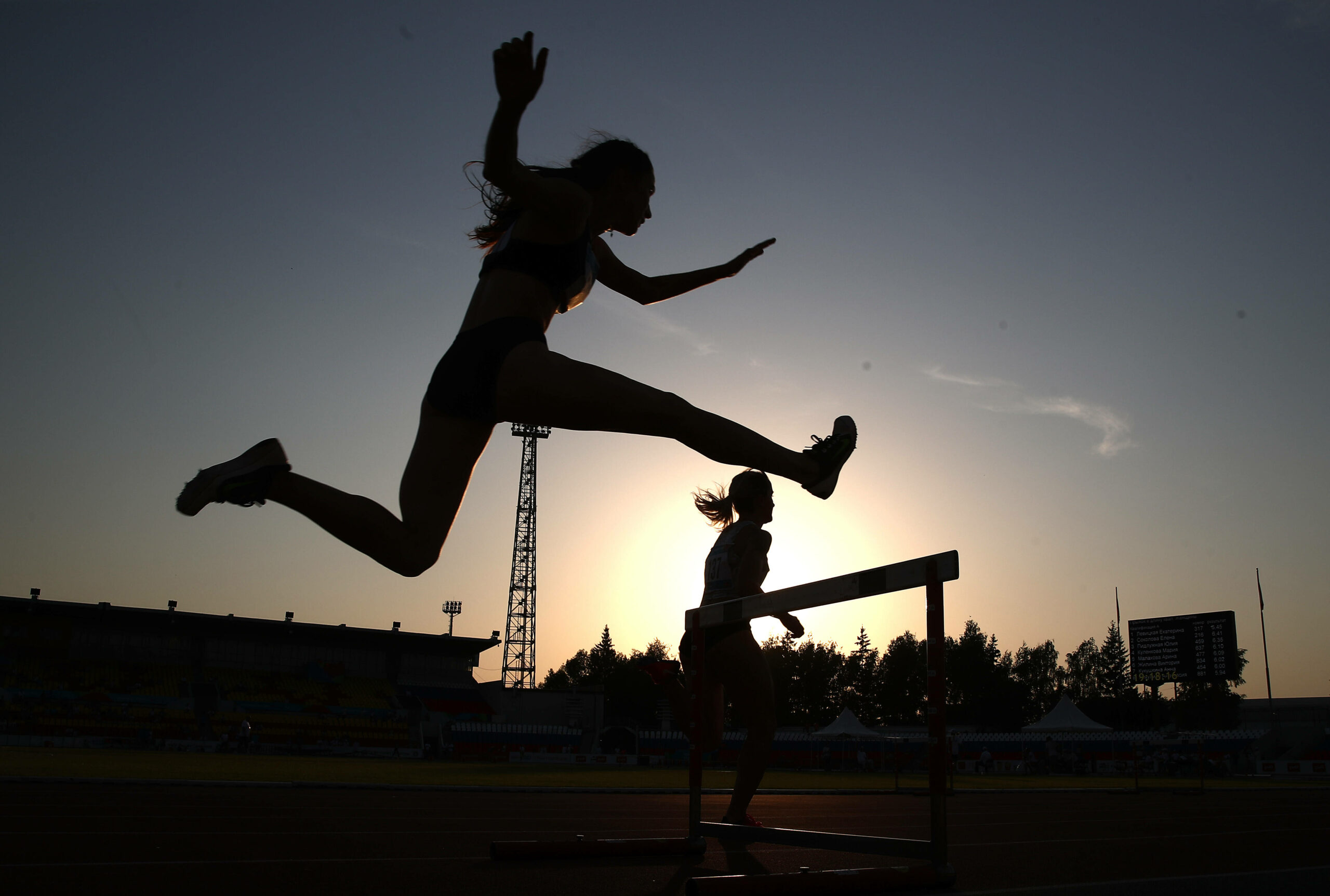 Zwei Leichtathletinnen beim Hürdenlauf. Nur Silhouetten sind erkennbar.