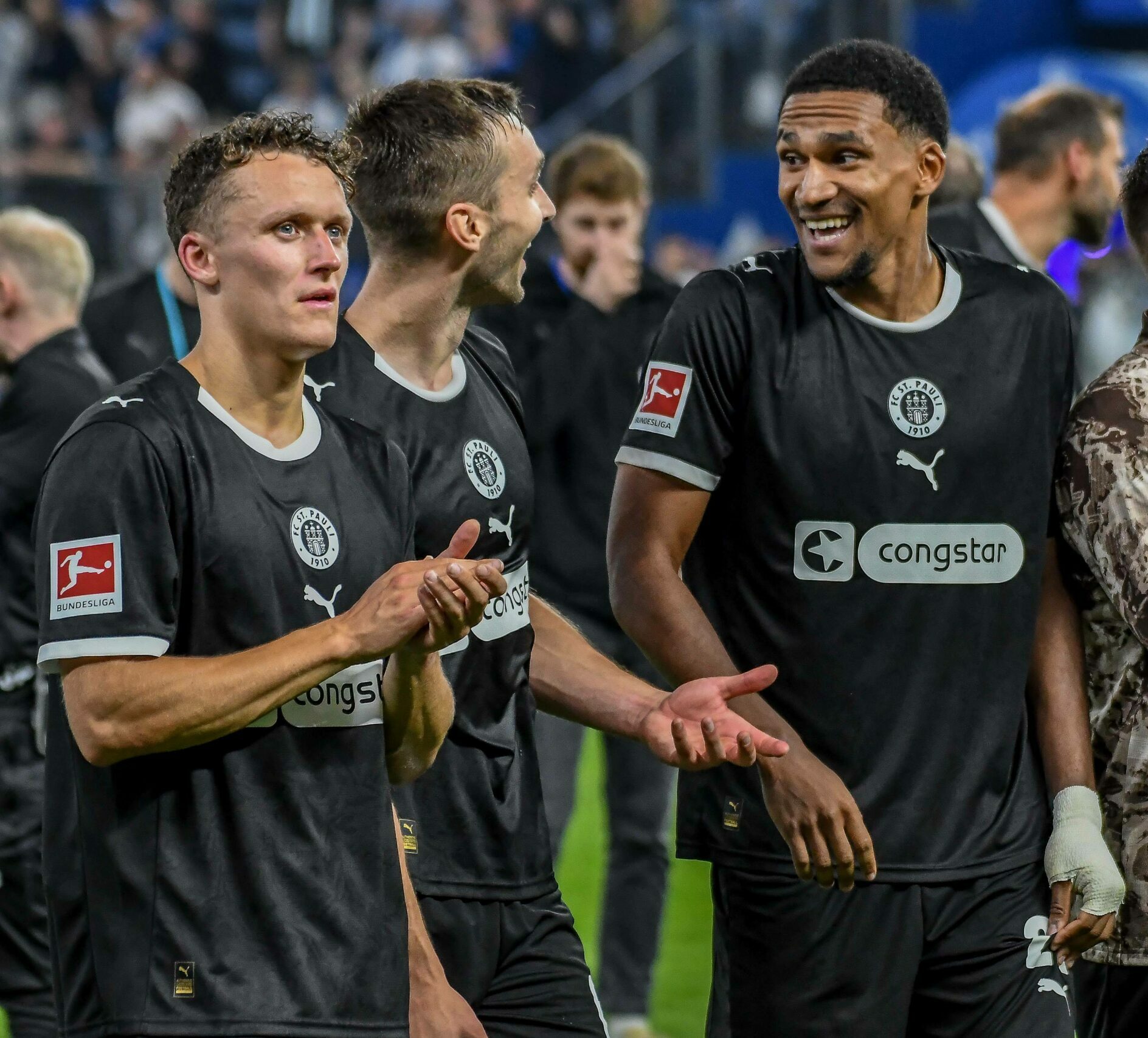 Martijn Kaars, James Sands und Andréas Hountondji stehen vor der Fankurve
