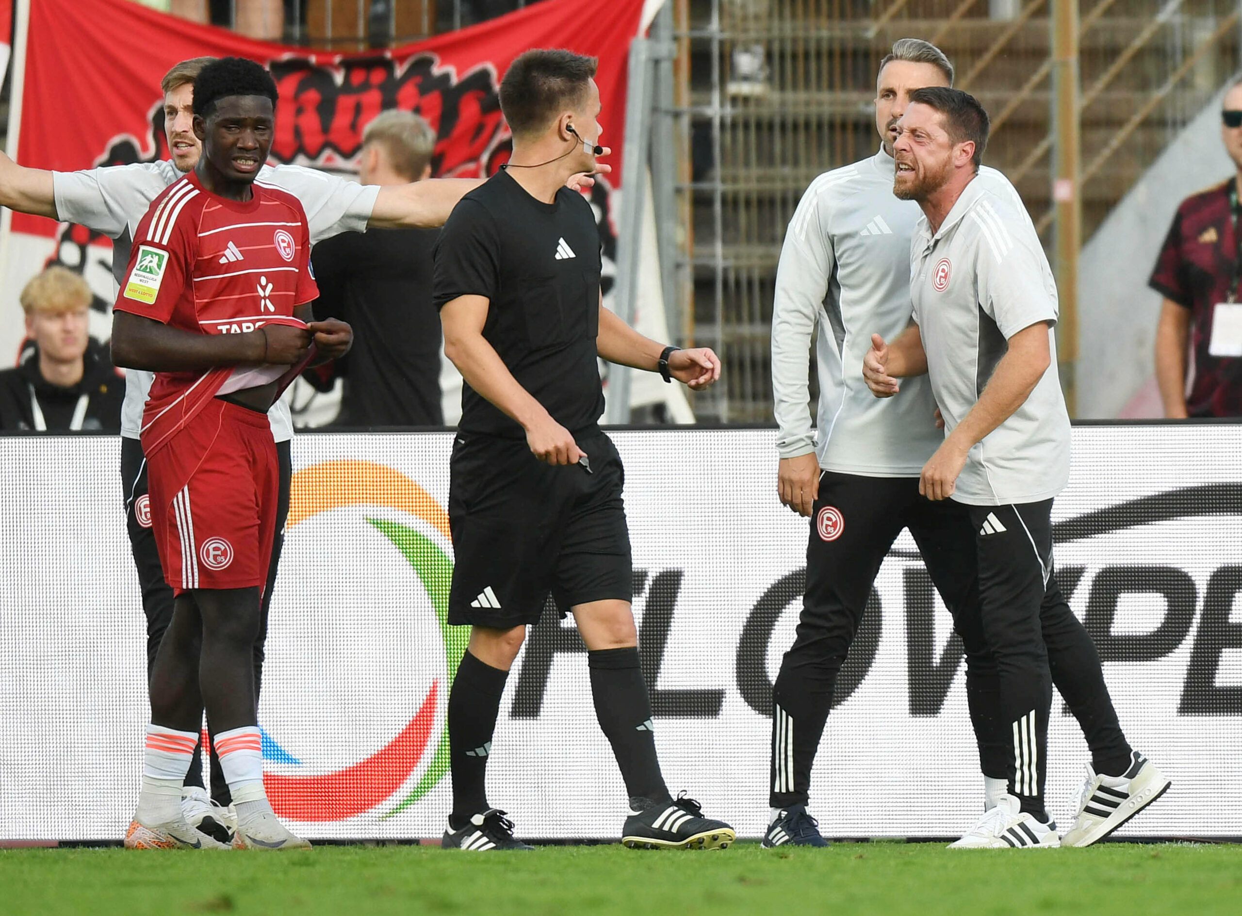 Quiala-Tito steht neben dem Schiedsrichter und den Fortuna Düsseldorf Betreuern inklusive Andreas Lambertz.