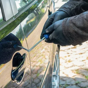 Eine Person versucht das Schloss einer Autotür aufzubrechen.