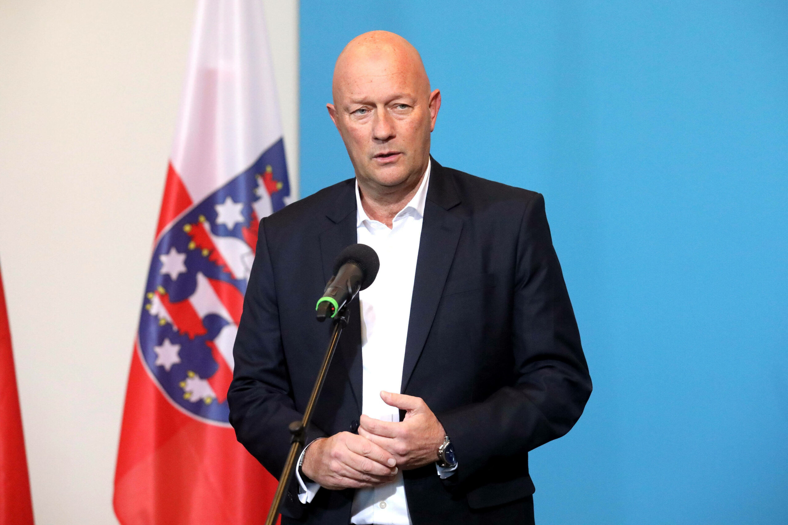 Thomas Kemmerich steht vor einer Flagge mit dem Thüringer Wappen an einem Mikrofon.