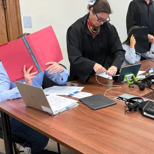 Peter O. hält sich eine rote Mappe vor das Gesicht. Seine Ehefrau Olga O. hält sich eine schwarze Laptop-Tasche vor ihr Gesicht.