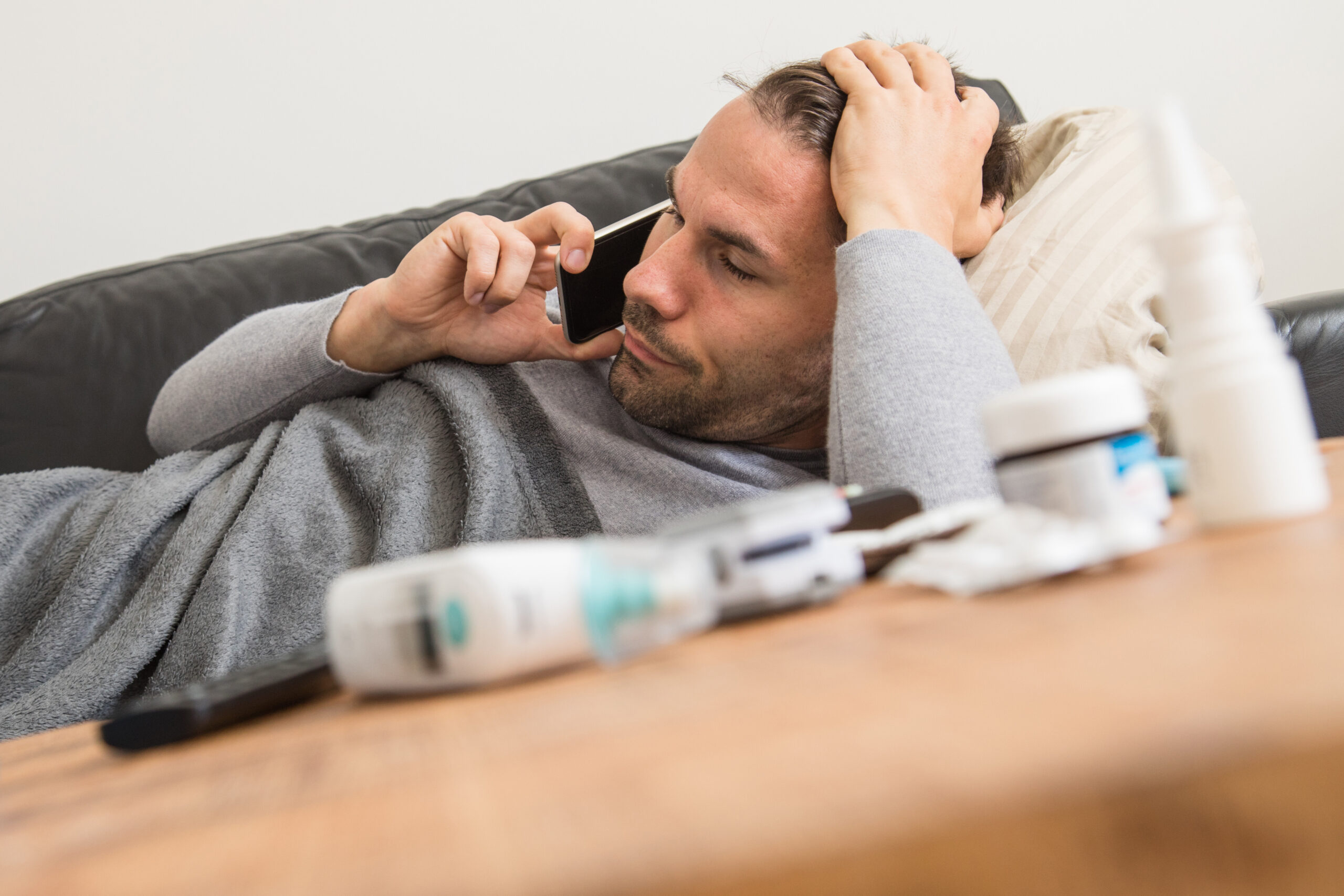 Mann liegt krank auf einem Sofa und telefoniert