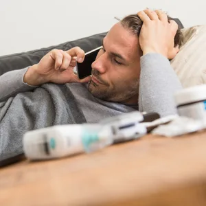 Mann liegt krank auf einem Sofa und telefoniert
