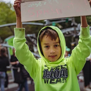 Ein Junge hält ein Schild in die Höhe. Darauf steht: „Wir brauchen unseren Spielplatz!“