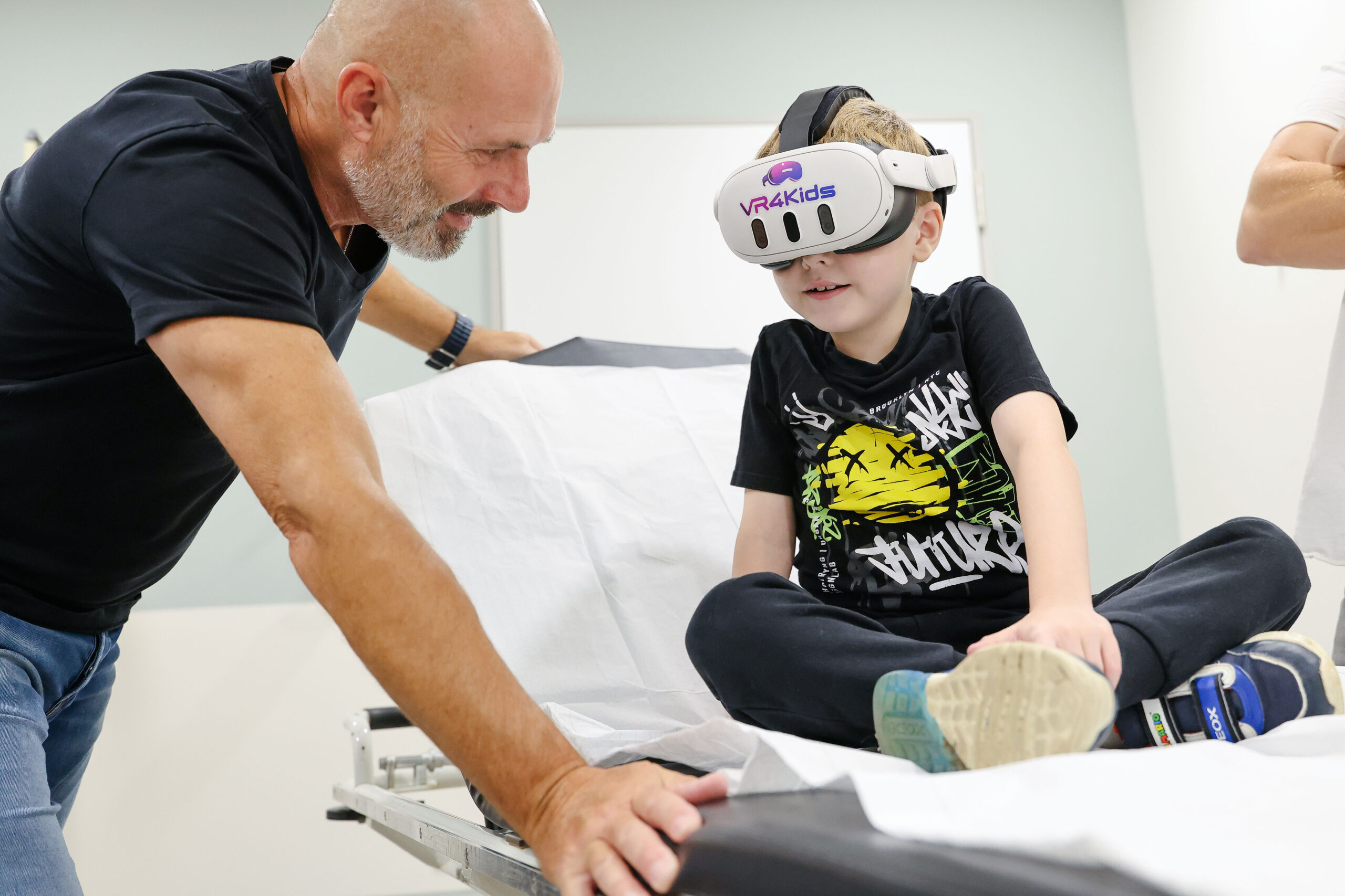 Kenan Bas (M.) schaut im München Klinikum Schwabing 360-Grad-Videos vom Oktoberfest mit einer Virtual-Reality-Brille von „VR4Kids“ und kann sich so von der Untersuchung ablenken.