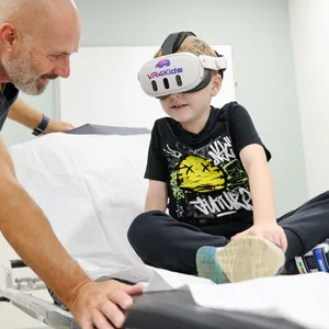 Kenan Bas (M.) schaut im München Klinikum Schwabing 360-Grad-Videos vom Oktoberfest mit einer Virtual-Reality-Brille von „VR4Kids“ und kann sich so von der Untersuchung ablenken.