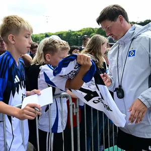 Trainer Merlin Polzin unterschreibt für einen Fan auf dem neuen HSV-Heimtrikot.