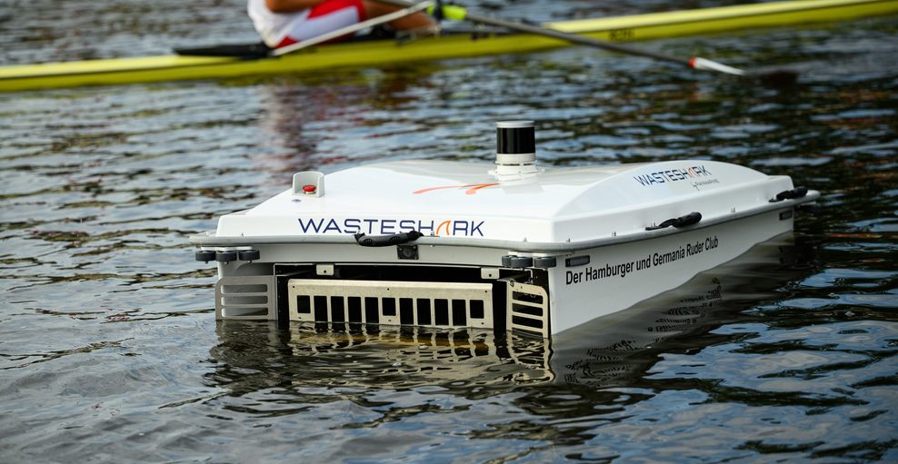 Der WasteShark schwimmt im Wasser. Er ist weiß und hat eine Rechteckige Form. Vorne hat er eine Öffnung um Abfall einzusammeln und Gitter, damit der eingesammelte Müll nicht wieder raus treibt.