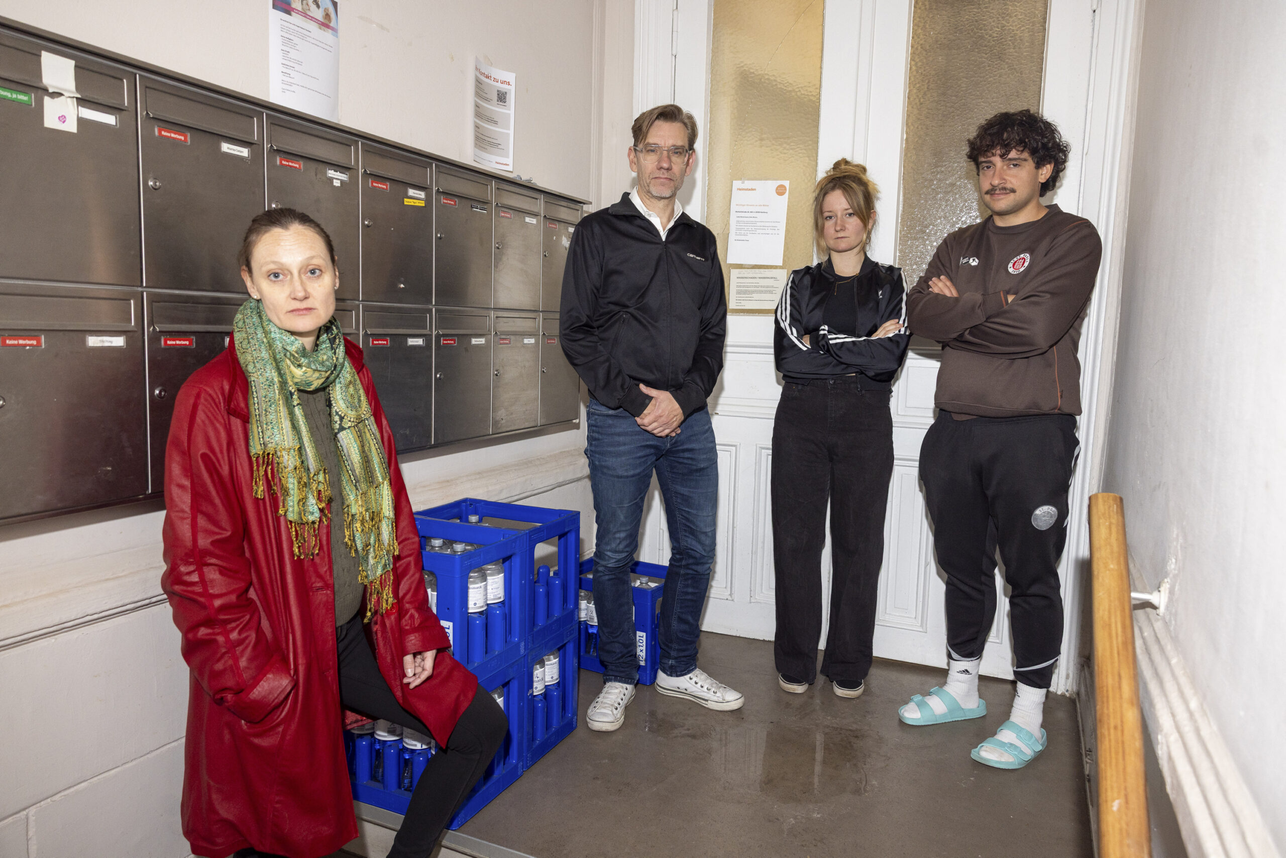 Die Mieterinnen und Mieter des Gebäudes an der Wohlwillstraße 48 – neben ihnen die paar Wasserkästen, die ihnen der Vermieter zur Verfügung gestellt hat. In der Mitte hat sich eine Pfütze gebildet.