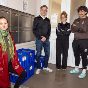 Die Mieterinnen und Mieter des Gebäudes an der Wohlwillstraße 48 – neben ihnen die paar Wasserkästen, die ihnen der Vermieter zur Verfügung gestellt hat. In der Mitte hat sich eine Pfütze gebildet.