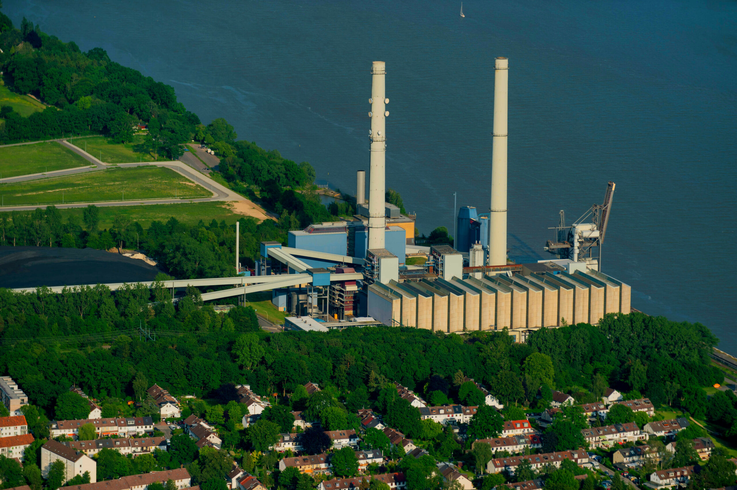 Luftbild vom Heizkraftwerk Wedel an der Elbe. Zu sehen sind die zwei Türme. Das Kraftwerk liegt direkt am Wasser und drum herum sind viele Bäume.