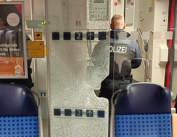 Ein Bundespolizist steht vor einer beschädigten Glastür in einer Regionalbahn.