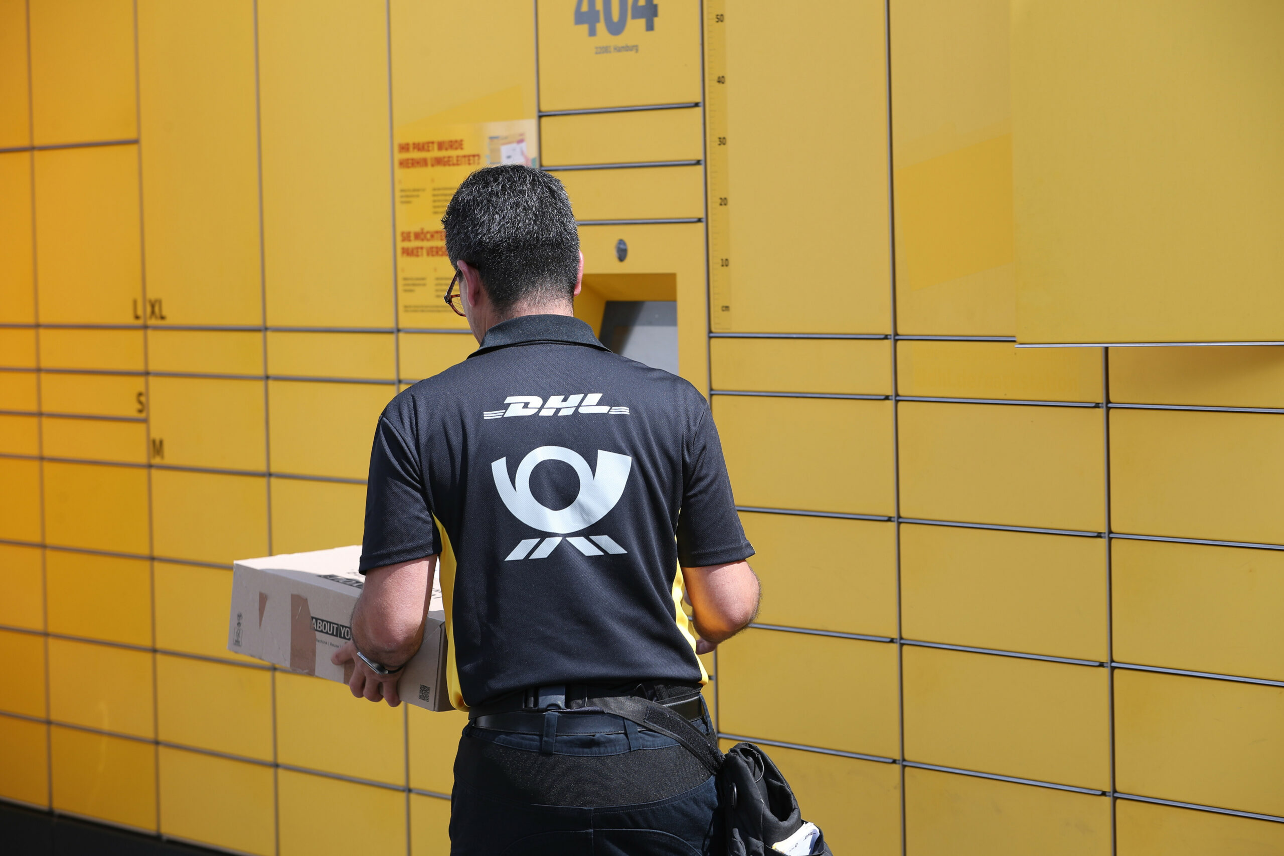 Ein Postbote der Deutschen Post steht vor einer DHL-Packstation.