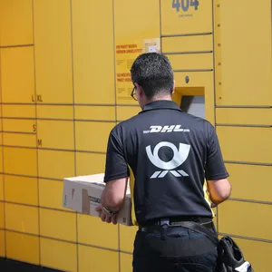 Ein Postbote der Deutschen Post steht vor einer DHL-Packstation.