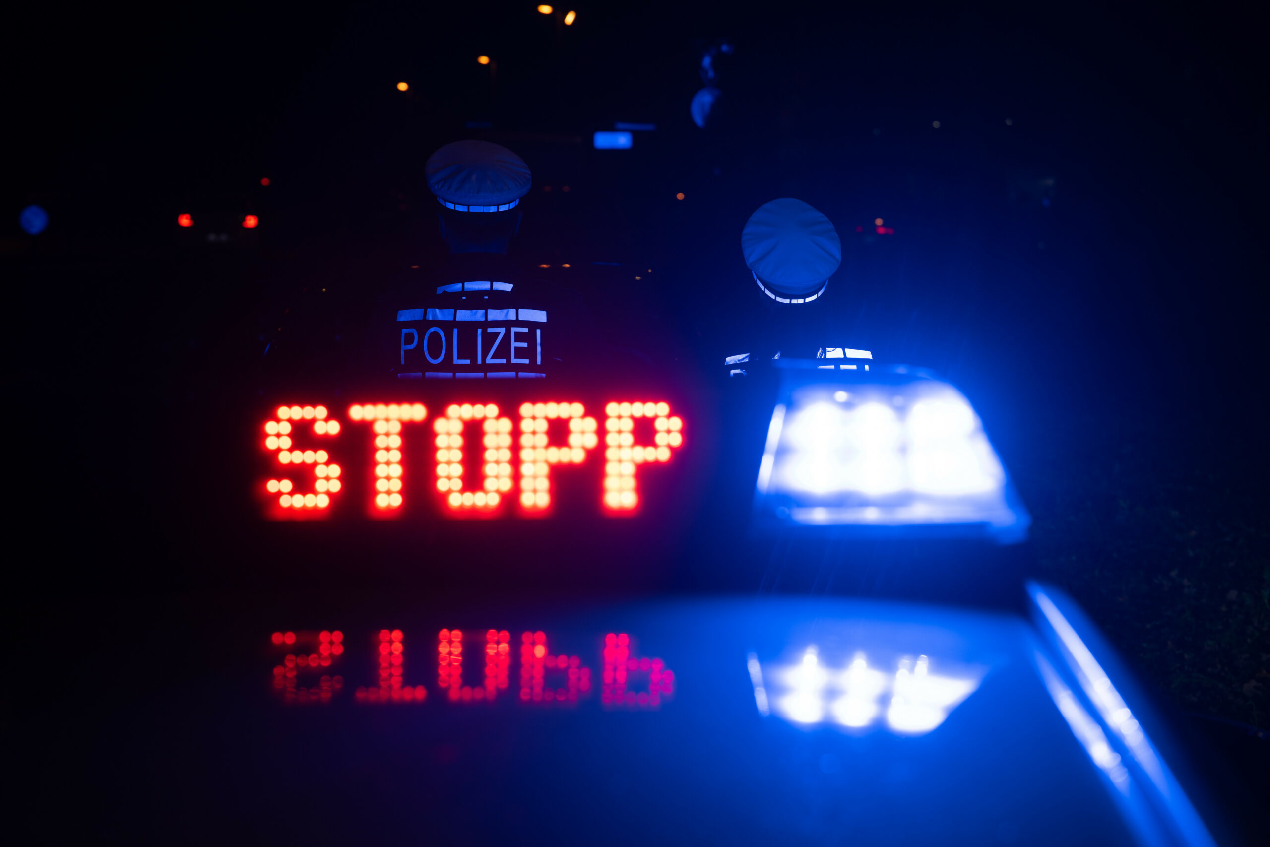 Zwei Polizisten stehen vor einem Polizeifahrzeug. Auf der Anzeigetafel steht „Stopp“..