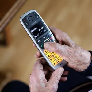Ältere Person mit Festnetz-Telefon in den Händen.