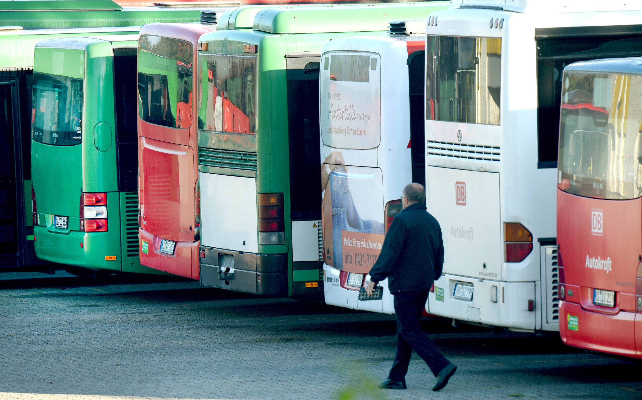Ein Busdepot mit mehreren parkenden Bussen. Ein Fahrer läuft im Vordergrund.