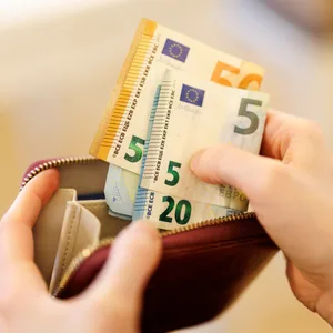 Hände die Geldscheine in ein Portemonnaie reintun.