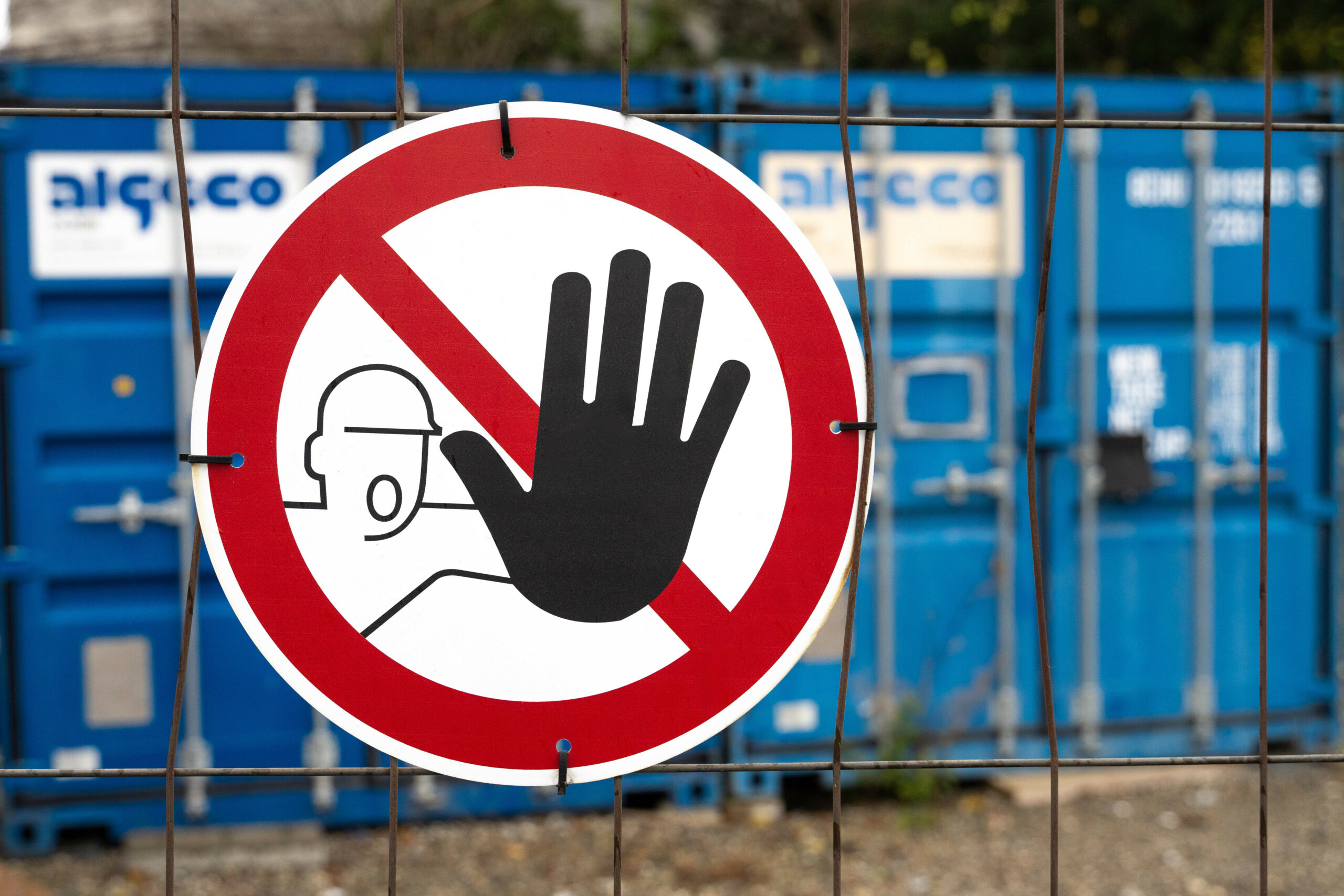 Verboten Schild vor einem blauen Container an einer Absperrung und Bauzaun.