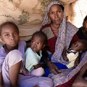 Eine Frau sitzt mit fünf Kindern in einem Zelt aus Tüchern.