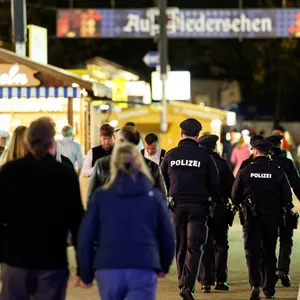 Polizisten gehen über das Gelände vom Oktoberfest in München. Im Hintergrund sind Buden der Wiesn.