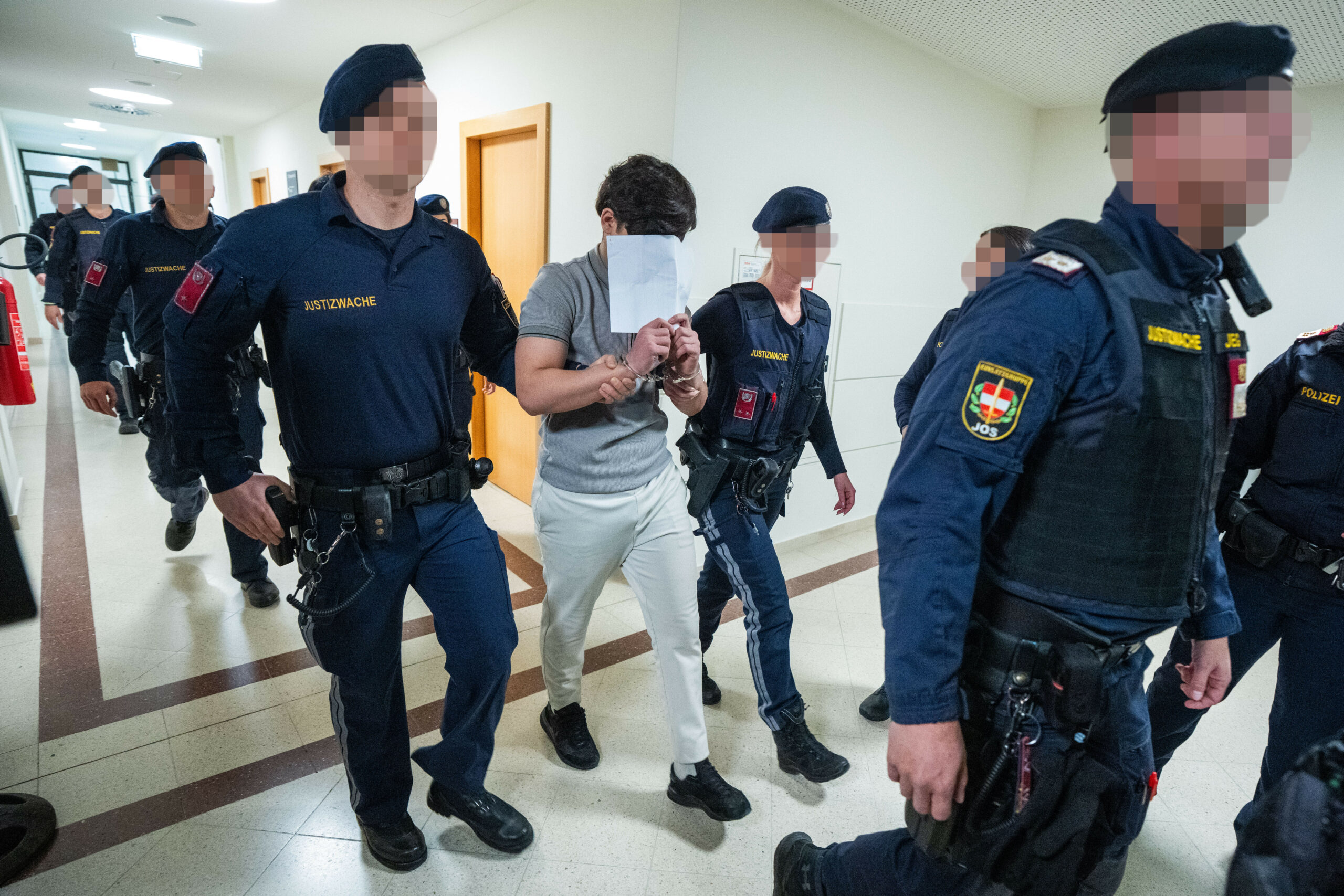 Ein Jugendlicher wird von Polizisten in den Gerichtssaal geführt. Er trägt Handschellen.