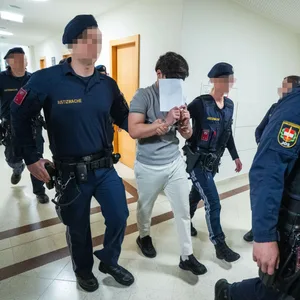 Ein Jugendlicher wird von Polizisten in den Gerichtssaal geführt. Er trägt Handschellen.