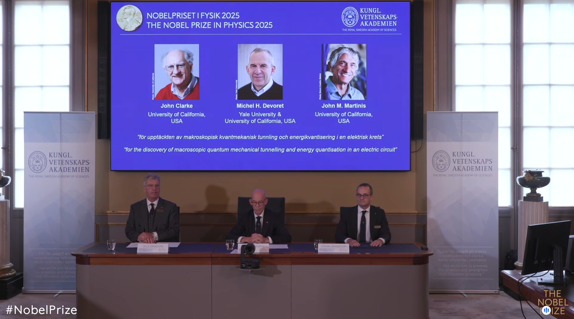 Standbild aus dem Livestream zur Bekanntgabe des Nobelpreises für Physik 2025: Auf einer Leinwand ist die Präsentation der diesjährigen Preisträger, die in den USA forschenden Quantenphysiker John Clarke (l-r), Michel Devoret und John Martinis, zu sehen.