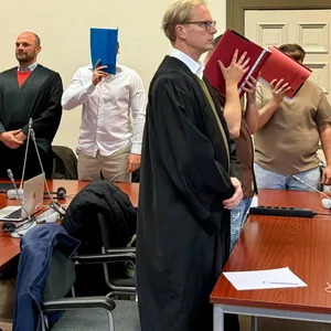 Die vier Angeklagten sitzen neben ihren Rechtsanwälten im Gerichtssaal.
