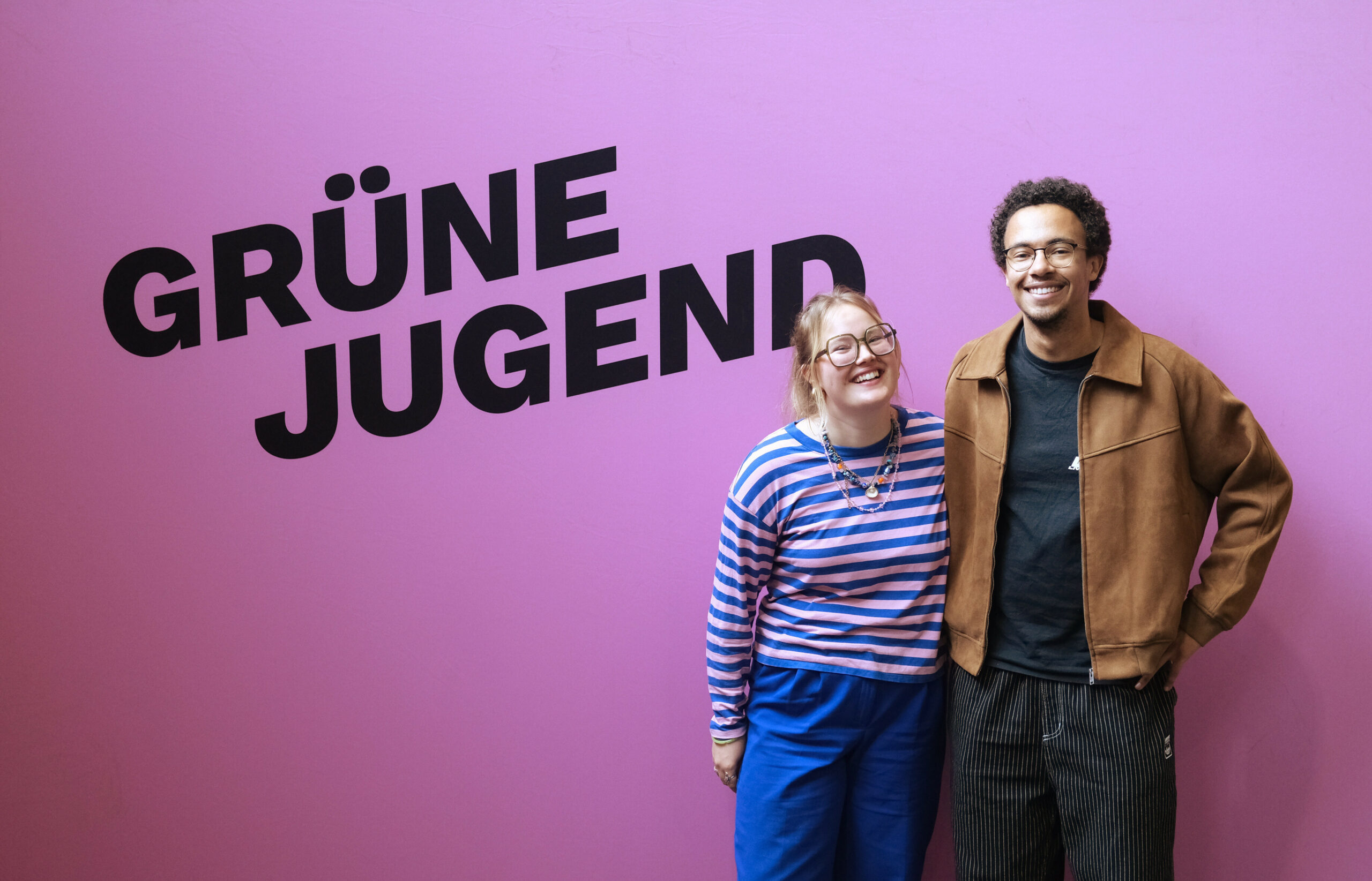 Henriette Held und Luis Bobga stehen vor einer rosa Wand auf der groß „Grüne Jugend“ steht.