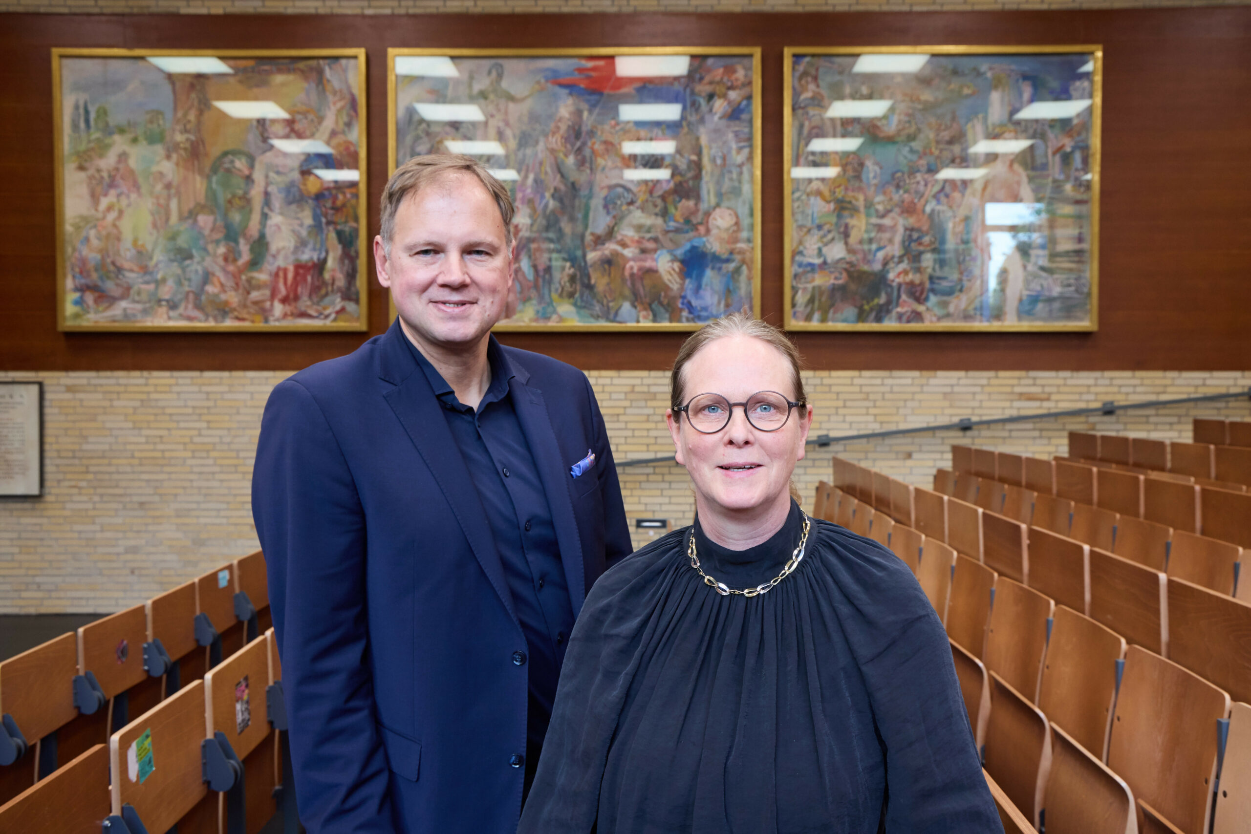 Hauke Heekeren, Präsident der Universität Hamburg und Antje Nagel, Sammlungsbeauftragte und Leitung Unimuseum, stehen vor drei Gemälden von Oskar Kokoschka, die jetzt an die Universität zurückgekehrt sind.