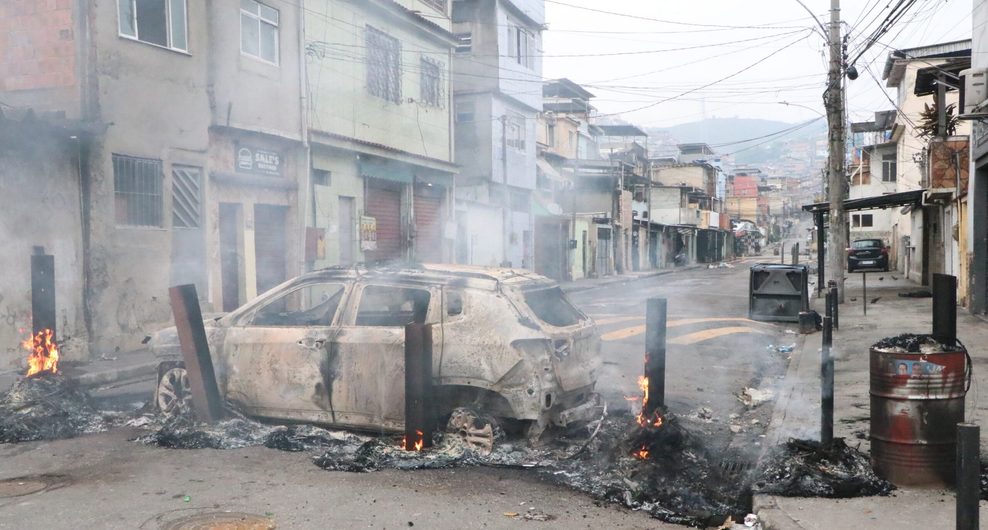 Das abgebrannte Auto steht quer auf der Straße um den Zugang zu den dort liegenden Favelas zu versperren.