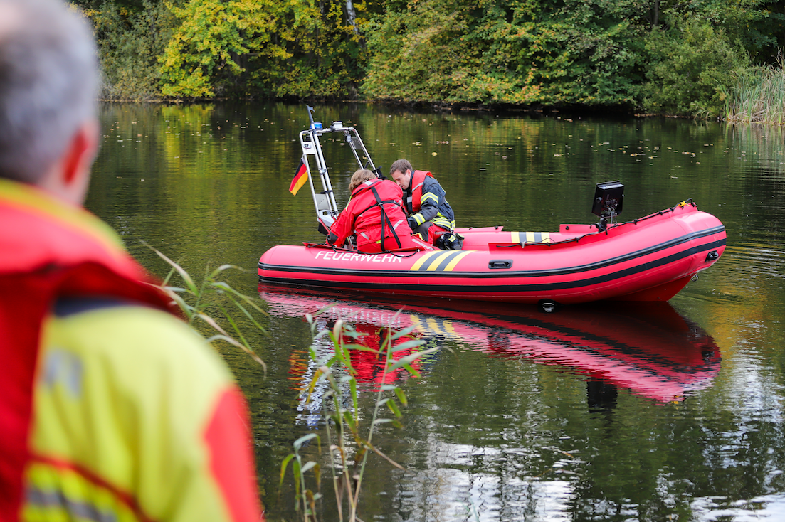 Zwei Feuerwehrmänner sitzen auf einem Boot der Feuerwehr und schauen ins Wasser.