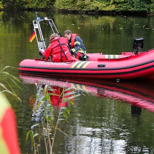 Zwei Feuerwehrmänner sitzen auf einem Boot der Feuerwehr und schauen ins Wasser.