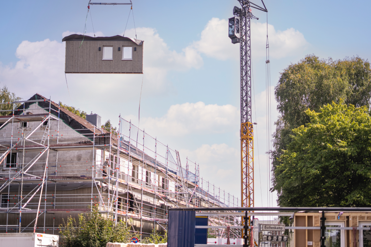 Ein Kran hebt Fassadenelemente zum Mehrfamilienhaus. So sollen klimaeffiziente Sanierungen günstiger und schneller erfolgen.Ein Kran hebt Fassadenelemente zum Mehrfamilienhaus. So sollen klimaeffiziente Sanierung günstiger und schneller erfolgen.