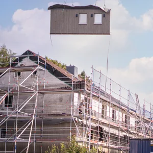 Ein Kran hebt Fassadenelemente zum Mehrfamilienhaus. So sollen klimaeffiziente Sanierungen günstiger und schneller erfolgen.Ein Kran hebt Fassadenelemente zum Mehrfamilienhaus. So sollen klimaeffiziente Sanierung günstiger und schneller erfolgen.