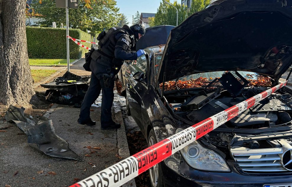 Ein Polizist steht an einem Pkw, der gebrannt hat, in der Nähe des Münchener Einfamilienhauses.