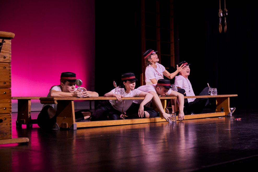 Fünf Schauspieler sitzen neben Sportgeräten auf der Bühne.