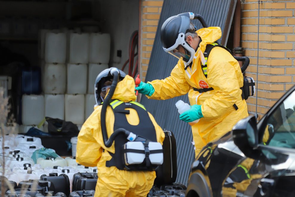 Ermittler in gelben Schutzanzügen mit Atemgeräten zwischen Dutzenden Fässern und Kanistern mit Chemikalien vor einem der durchsuchten Häuser im Kreis Pinneberg.